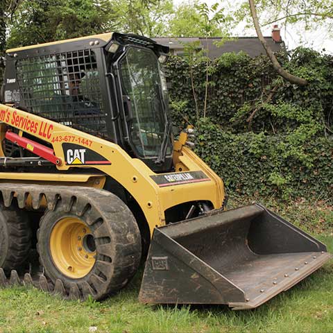 A Caterpillar skid steer, also known as a Bobcat, moves through a grassy lot with a digging bucket attached